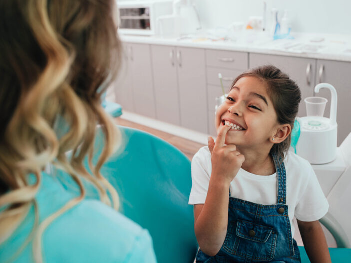 Young-girl-smiling-and-pointing-to-her-teeth-at-dental-office